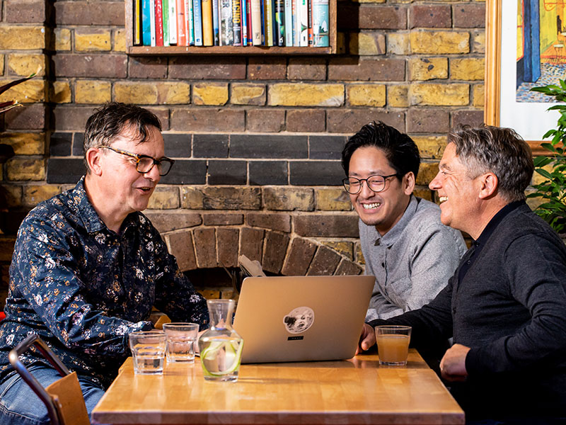 Three men looking at a laptop in a cafe